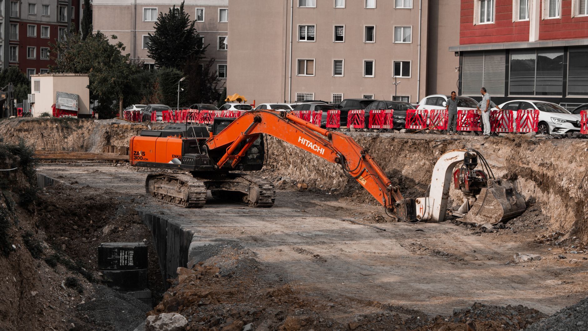 En orange grävmaskin utför markarbete på en byggarbetsplats i ett bostadsområde.